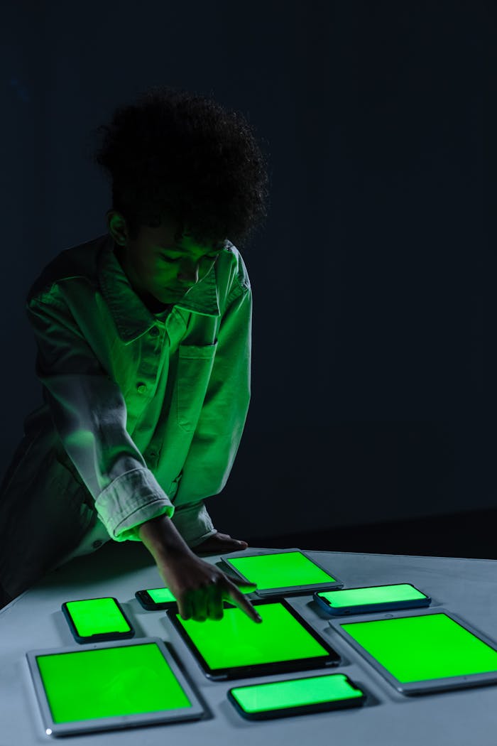 digital A child in a dark room interacts with several digital screens, glowing green, illustrating modern technology use.