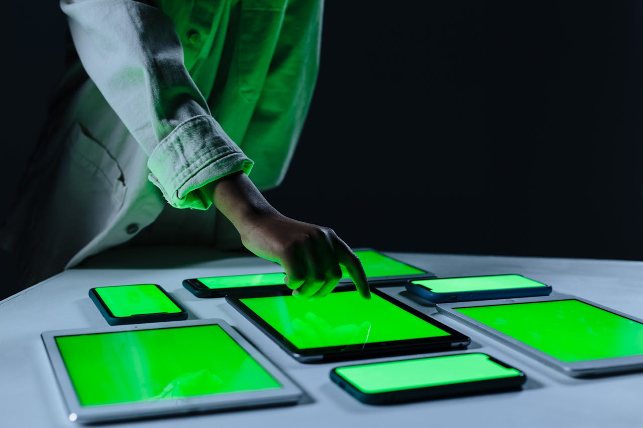 creative Hand interacting with multiple digital tablets on a green screen setup indoors.